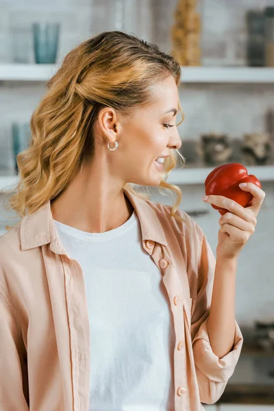 Attractive young woman holding red ripe bell pepper at kitchen — Stock Photo