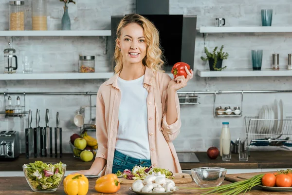 Attraktive junge Frau mit Paprika blickt beim Kochen in der Küche in die Kamera — Stockfoto