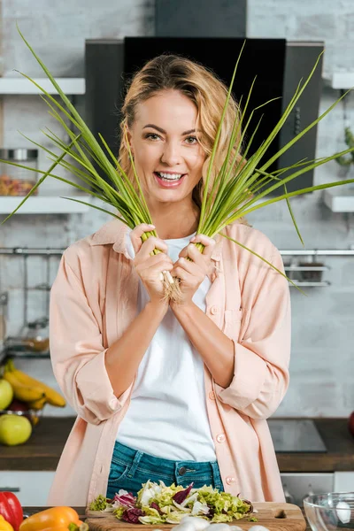 Glückliche junge Frau mit Porree blickt beim Kochen in der Küche in die Kamera — Stockfoto