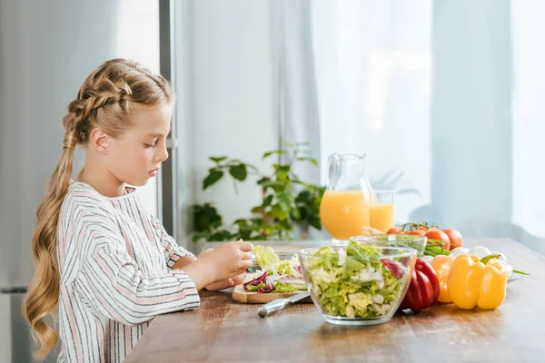 Seitenansicht eines konzentrierten kleinen Kindes, das in der Küche Salat zubereitet — Stockfoto