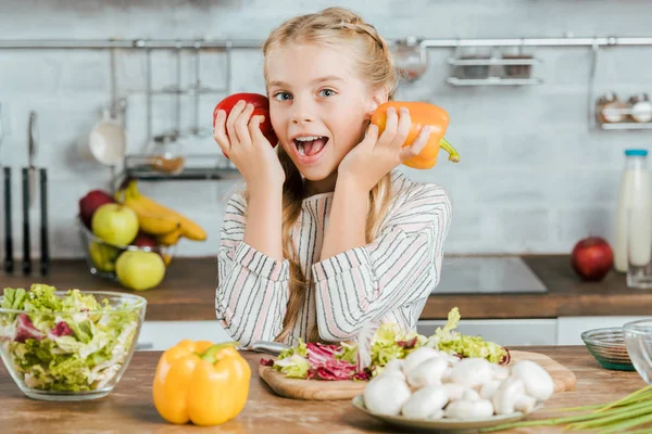 Happy little child with bell peppers looking at camera while making salad at kitchen — Stock Photo