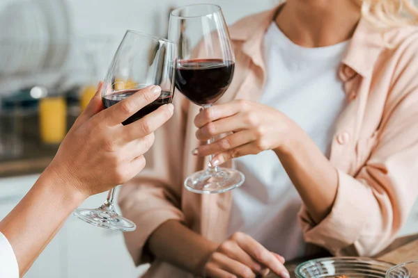 Recortado tiro de las mujeres tintineo con copas de vino tinto - foto de stock