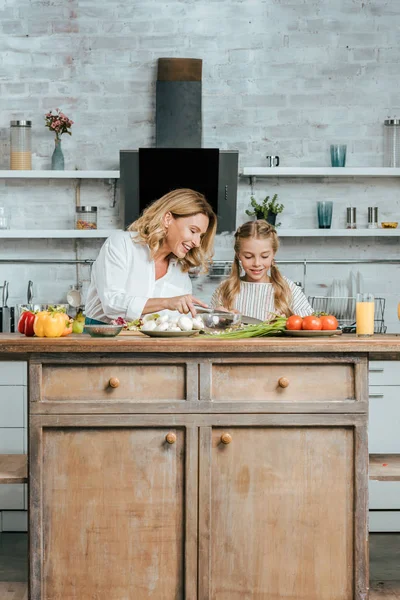 Smiling adult mother and little daughter cutting lettuce for salad together at home — Stock Photo