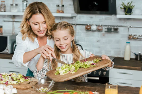 Bela mãe adulta e pequena filha fazendo salada juntos em casa — Fotografia de Stock