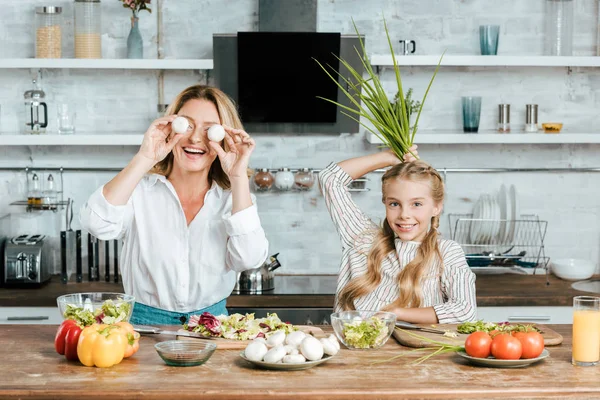 Sorrindo mãe e filha brincando com comida enquanto cozinhava olhando para a câmera em casa — Fotografia de Stock