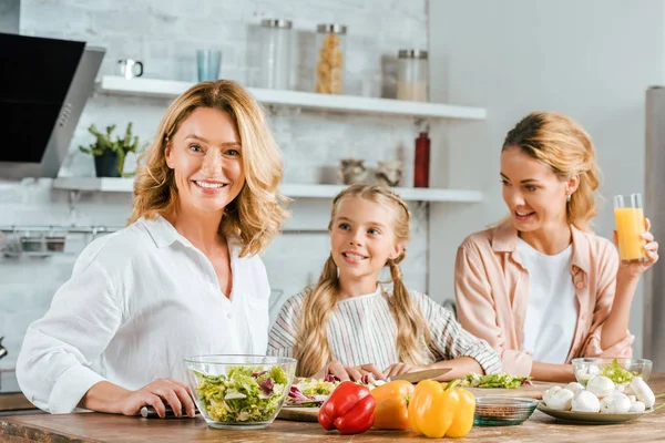 Adult woman cutting vegetables for salad with daughter and granddaughter at home — Stock Photo