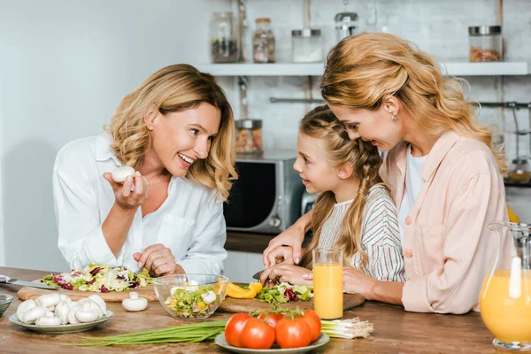 Kind schneidet Gemüse für Salat mit Mutter und Großmutter zu Hause und plaudert — Stockfoto