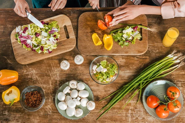 Foto recortada de mujeres y niños cortando verduras para ensalada en mesa rústica - foto de stock
