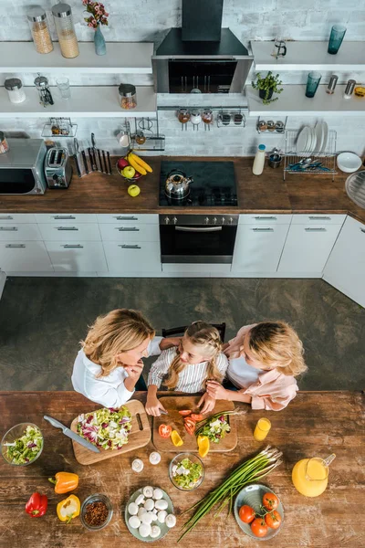 Вид сверху на ребенка резки овощей для салата с матерью и бабушкой на кухне — стоковое фото