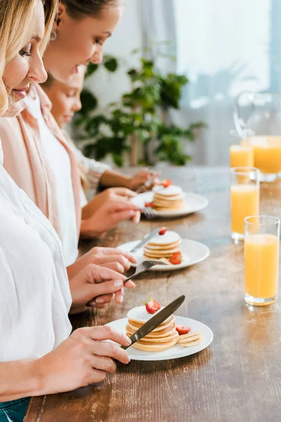 Side view of child with mother and grandmother eating pancakes for breakfast together at home — Stock Photo