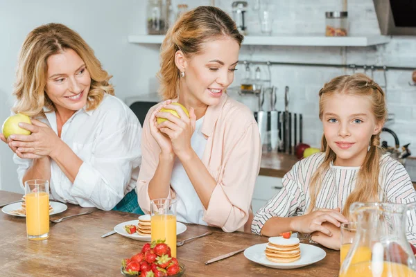 Glückliches kleines Kind mit Mutter und Großmutter, die Pfannkuchen zum Frühstück zu Hause essen — Stockfoto