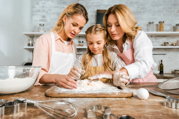 Adorable child with mother and grandmother making dough with flour and egg together at home — Stock Photo