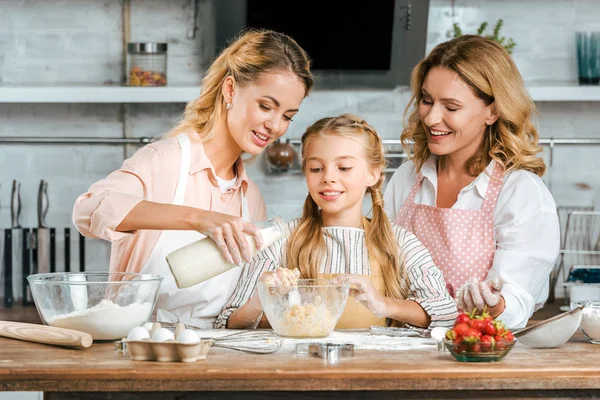 Усміхнена дитина з матір'ю і бабусею робить тісто разом вдома — стокове фото