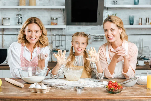 Glückliches kleines Kind, das mit Mutter und Großmutter zu Hause Teig backt und in die Kamera schaut — Stockfoto