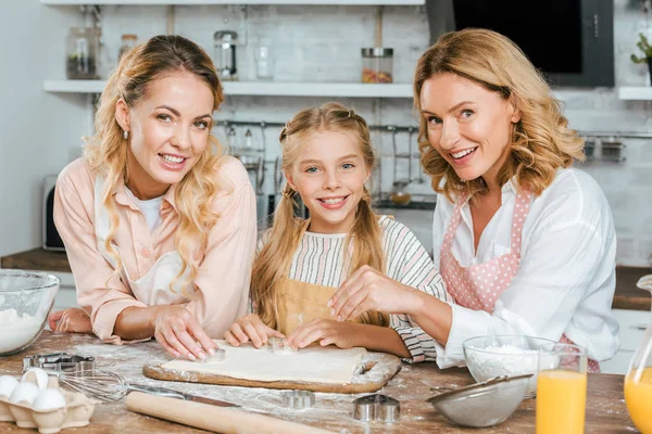 Belle felici tre generazioni di donne che fanno pasta insieme a casa e guardando la fotocamera — Foto stock