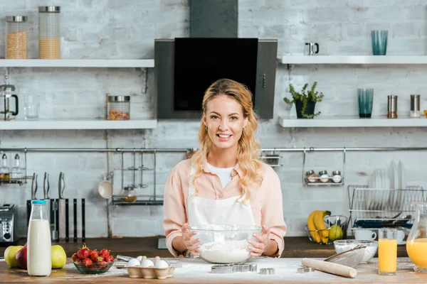 Lächelnde junge Frau mit Schüssel Teig blickt in die Küche — Stockfoto