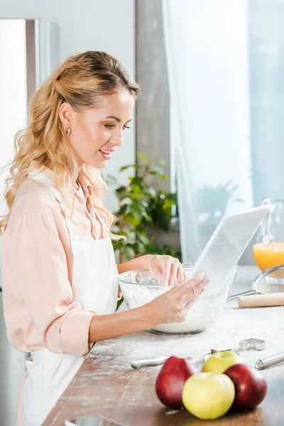 Attractive young woman making dough and using tablet at home — Stock Photo