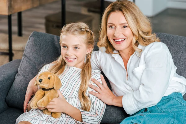 Happy mother and daughter sitting on couch and looking away — Stock Photo