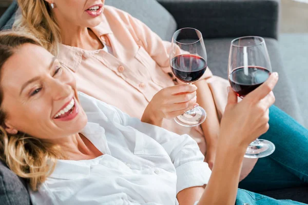 Tiro recortado de la madre madura y la hija adulta con copas de vino tinto pasar tiempo juntos en casa - foto de stock