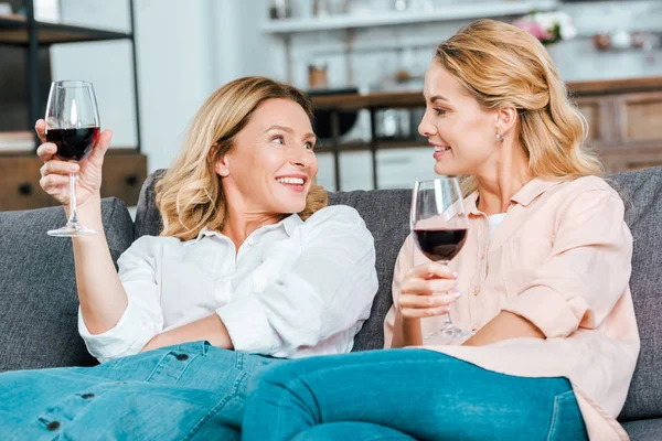 Madre madura feliz e hija adulta con copas de vino tinto pasar tiempo juntos en casa - foto de stock