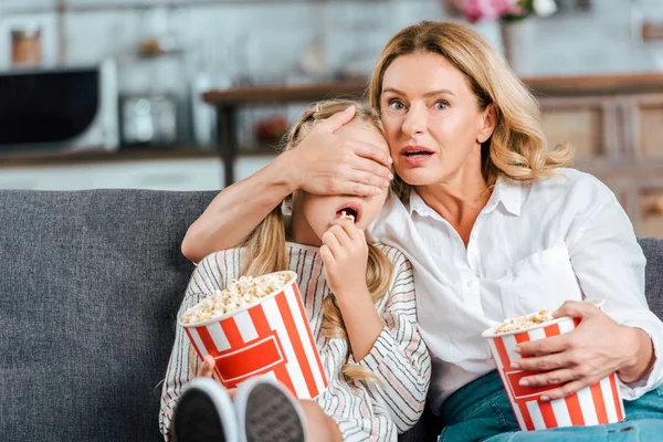 Испуганные мать и дочь с ведрами попкорна смотреть страшное кино дома — стоковое фото