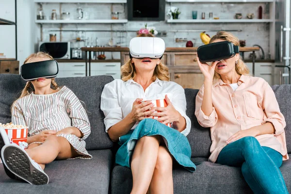 Kind mit Mutter und Großmutter, die zusammen auf der Couch sitzen und zu Hause Filme mit Virtual-Reality-Headsets ansehen — Stockfoto
