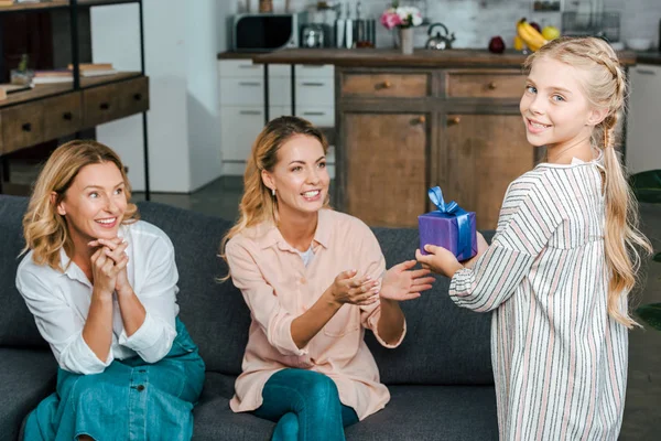 Entzückendes kleines Kind beschenkt Mutter, während sie mit Großmutter auf der Couch sitzt — Stockfoto