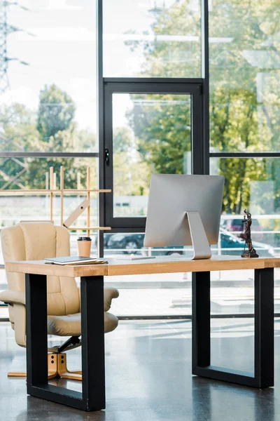 Sessel, Tisch mit Computer, Einweg-Kaffeetasse und Themis-Statue im Büro — Stockfoto