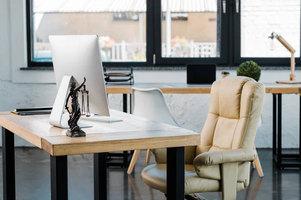 Armchair, table with computer and themis statue in business office — Stock Photo