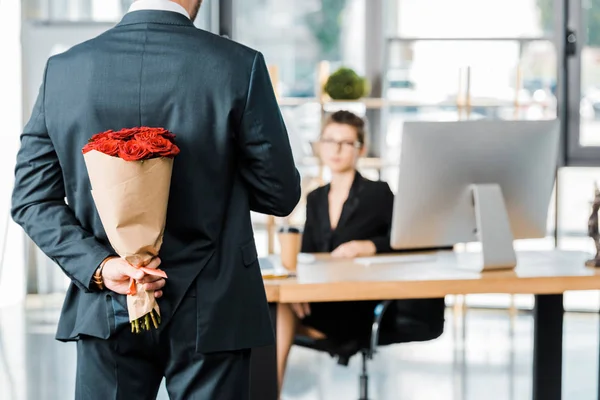 Imagen recortada de hombre de negocios escondiendo ramo de rosas detrás de la espalda para sorprender a la mujer de negocios en el cargo - foto de stock