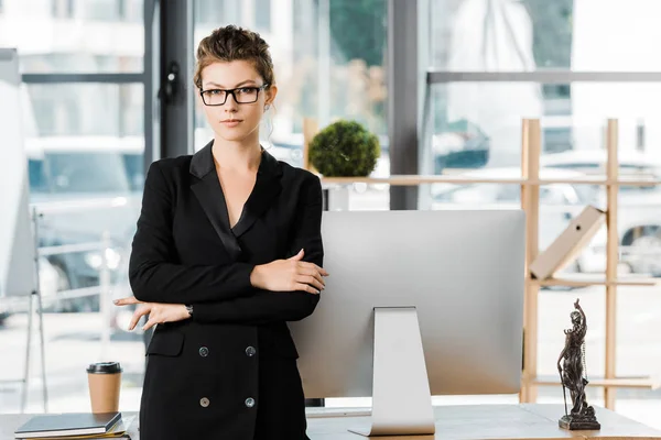 Portrait of attractive businesswoman standing with crossed arms and looking at camera in office — Stock Photo