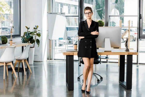 Beautiful businesswoman standing with crossed arms and looking at camera in office — Stock Photo