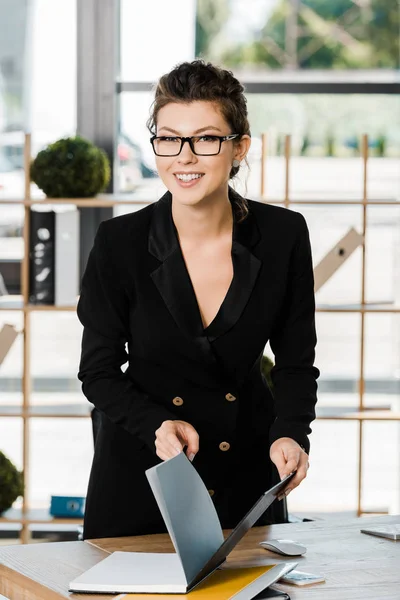 Donna d'affari attraente sorridente che tiene la cartella con documenti e guarda la macchina fotografica in ufficio — Foto stock