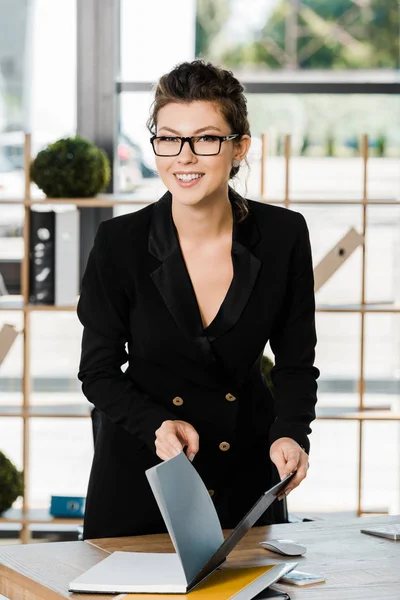 Souriant attrayant femme d'affaires tenant dossier avec des documents et regardant la caméra dans le bureau — Photo de stock