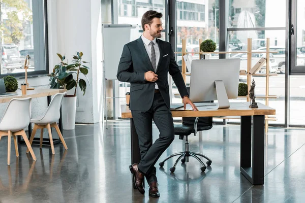Handsome businessman standing near table in office and looking away — Stock Photo