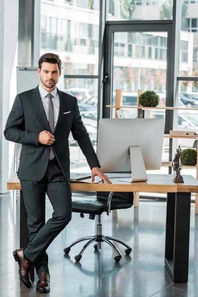 Schöner Geschäftsmann, der im Büro am Tisch steht und in die Kamera schaut — Stockfoto