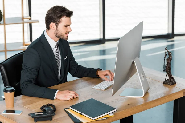 Vista lateral del hombre de negocios guapo que trabaja con la computadora en la mesa en la oficina - foto de stock