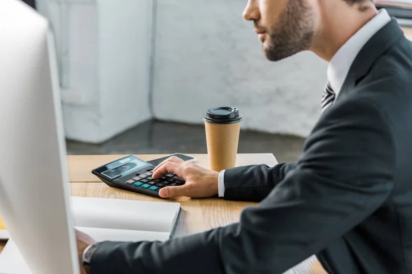 Imagen recortada de hombre de negocios utilizando la calculadora en la oficina, carpeta abierta en la mesa - foto de stock