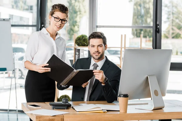 Businesswoman and businessman holding folder with documents in office and looking at camera — Stock Photo