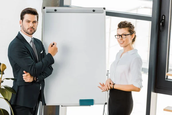 Portrait of young business colleagues standing at empty white board in office — Stock Photo