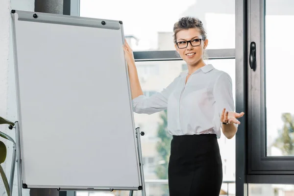 Портрет улыбающейся деловой женщины в очках, стоящей у белой доски в офисе — стоковое фото