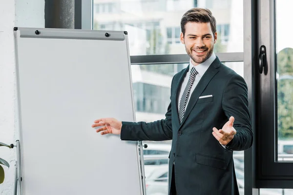 Retrato de hombre de negocios alegre en traje de pie en la pizarra blanca vacía en la oficina - foto de stock