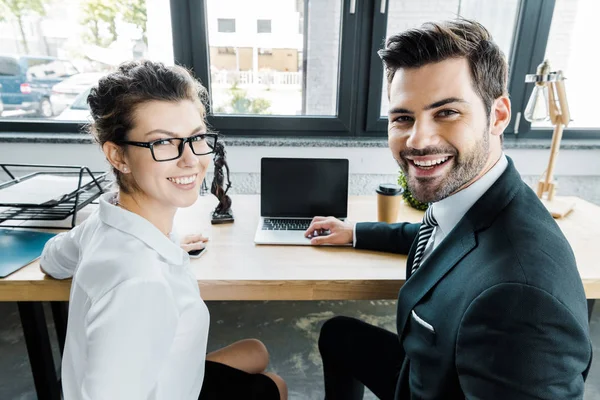 Avocats souriants sur le lieu de travail avec ordinateur portable avec écran blanc et femida au bureau — Photo de stock