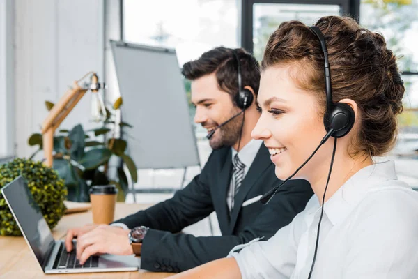 Vista laterale di operatori di call center sorridenti sul posto di lavoro in ufficio — Foto stock