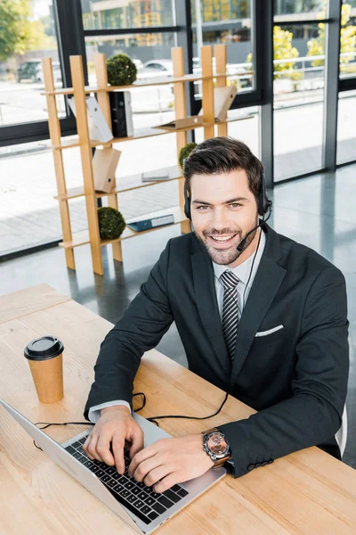 Operatore di call center sorridente con auricolare sul posto di lavoro con laptop in ufficio — Foto stock