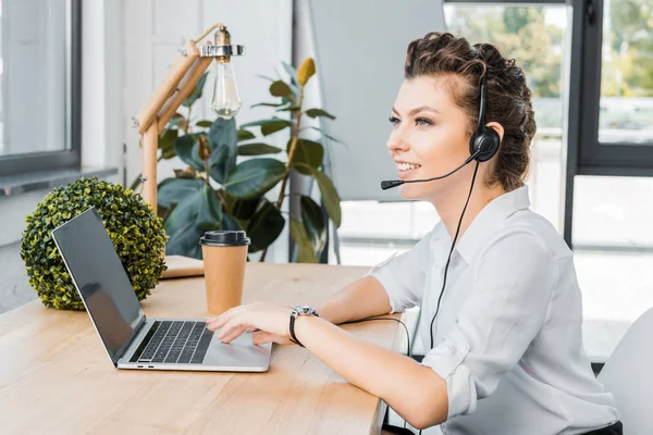 Side view of smiling female call center operator with headset at workplace in office — Stock Photo