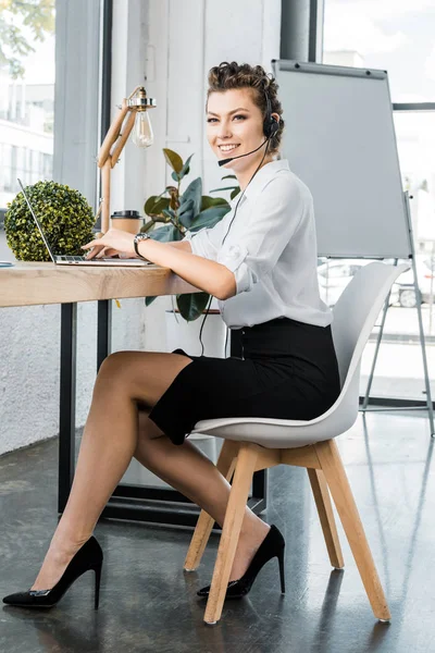 Молодая улыбающаяся женщина оператор колл-центра с гарнитурой на рабочем месте в офисе — стоковое фото