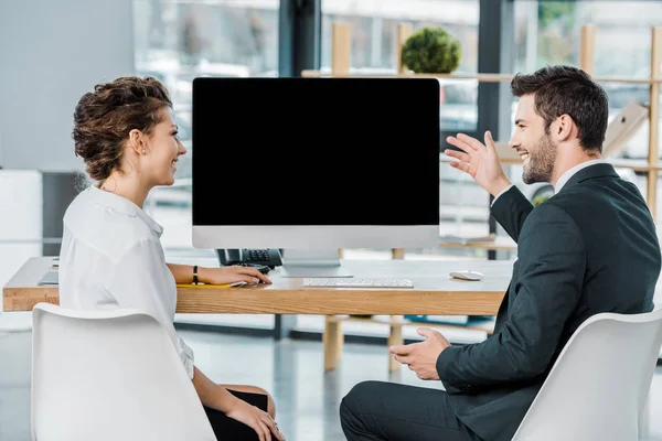 Colegas de negocios sonrientes teniendo discusión en el lugar de trabajo con la pantalla del ordenador en blanco en la oficina - foto de stock