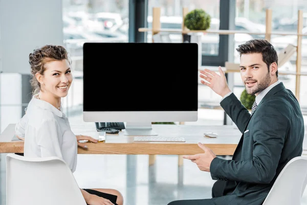 Jóvenes colegas de negocios sonrientes en el lugar de trabajo con pantalla de computadora en blanco en la oficina - foto de stock
