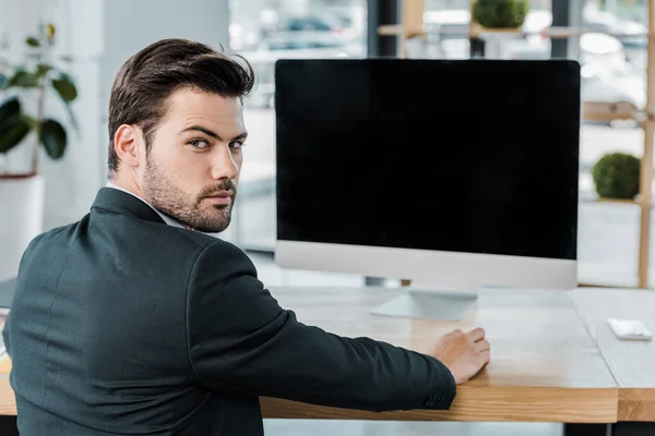 Back view of businessman at workplace with computer screen with blank screen in office — Stock Photo